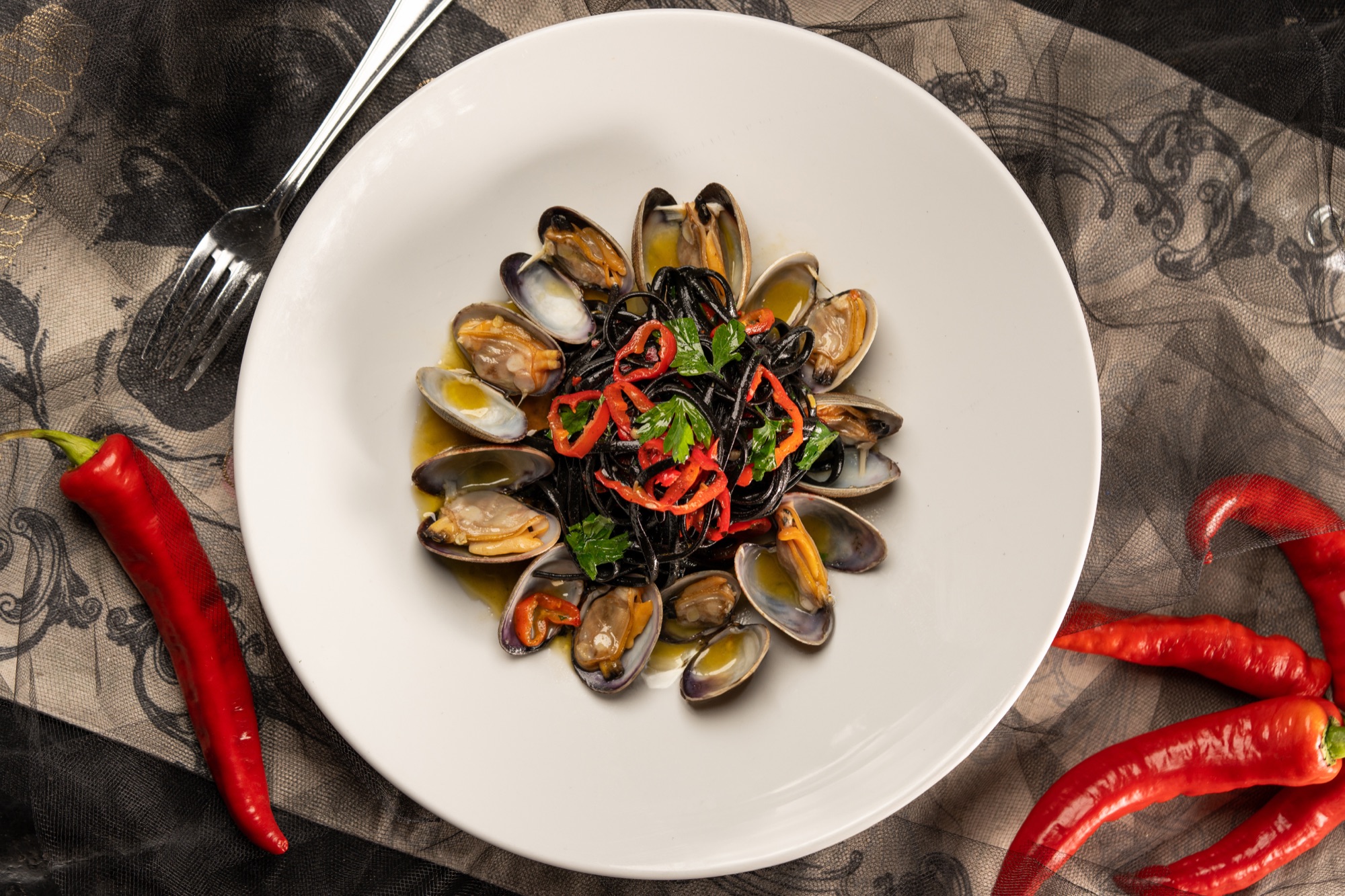 Squid ink pasta with clams from above, ringed by red chilies