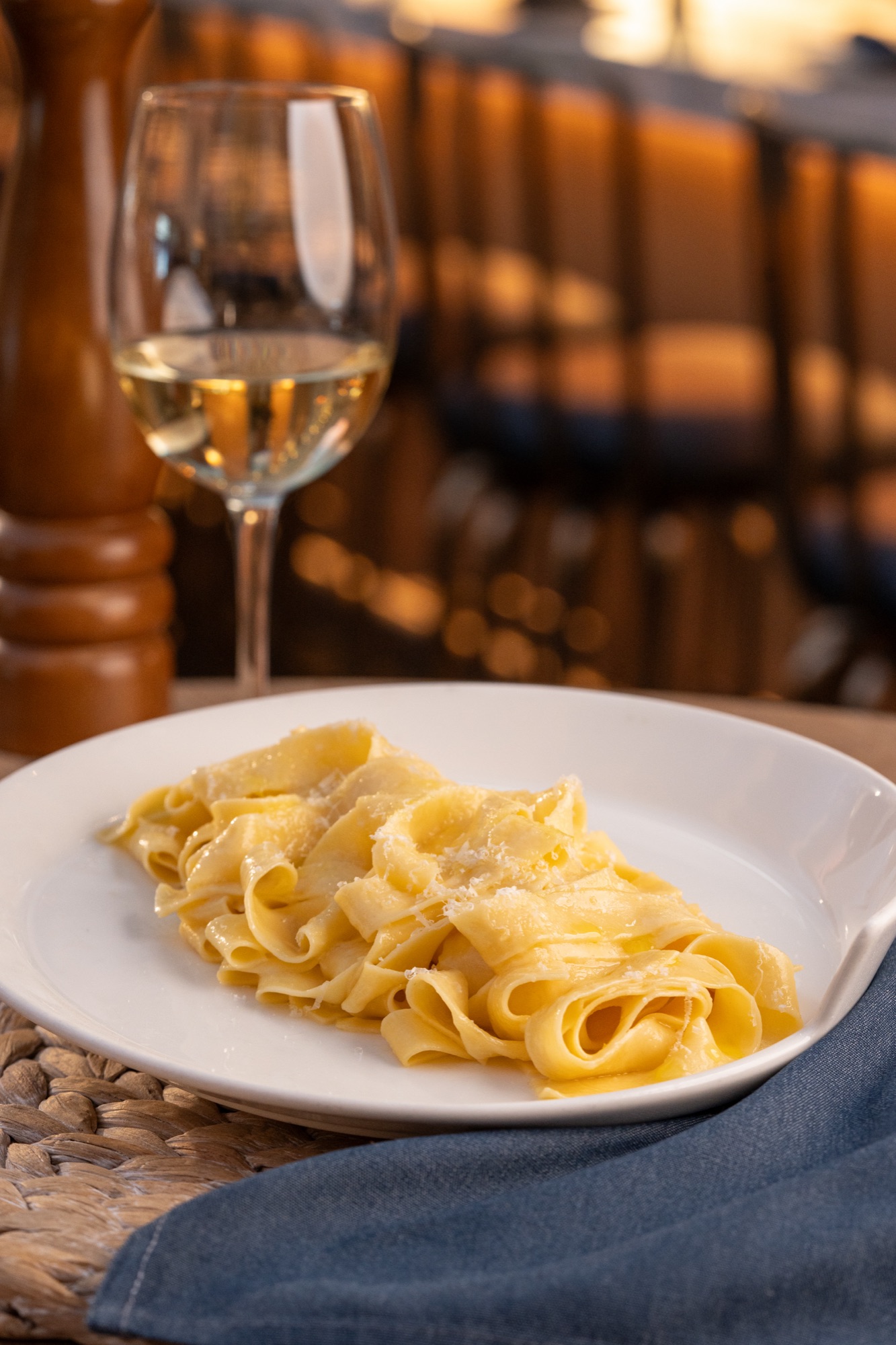 Pappardelle with parmigiano on a white plate, a pepper mill behind